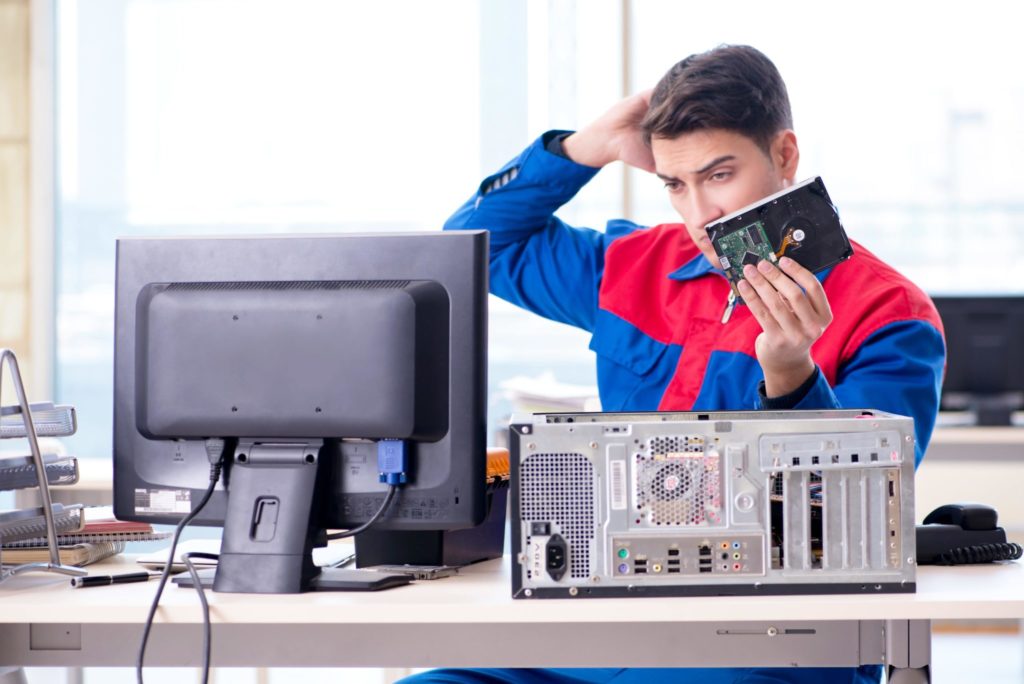 Young man removing hard drive from computer tower.